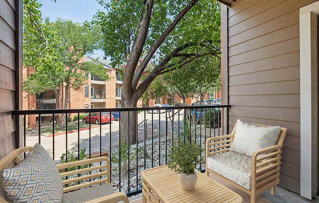 A balcony with a chair, a cushion, a table and a potted plant.