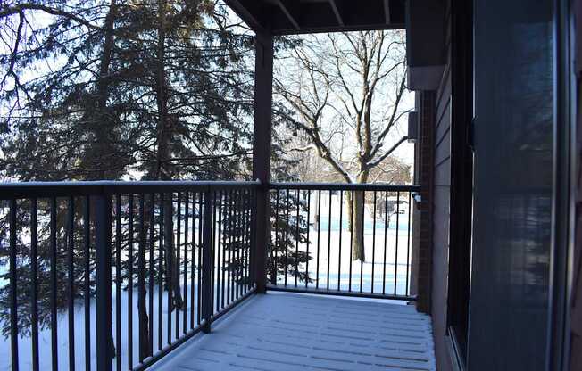 A snowy deck with a black railing and trees in the background.