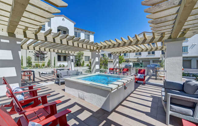 A pool surrounded by red chairs and wooden pergolas.