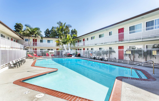 Outdoor swimming pool with sun chairs, a lounge area lined with apartments, and palm trees at Pacific Sands, San Diego, CA