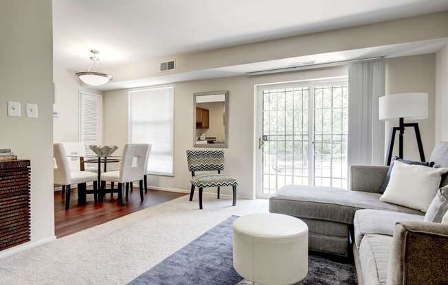 A well-lit living room with a grey couch and a white ottoman.