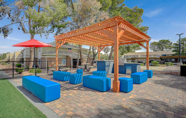 A pavilion with a red umbrella and blue seating is surrounded by trees.