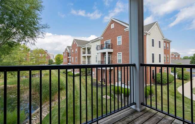 A balcony with a black railing overlooks a grassy area and a body of water.