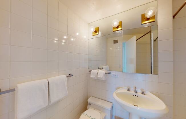 a bathroom with white tiles and a white sink with a mirror above it