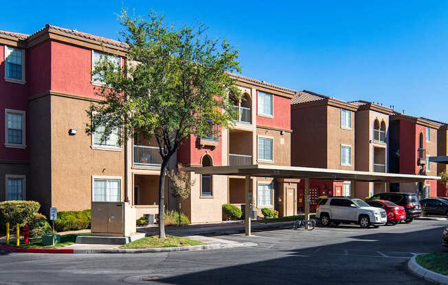 A row of apartment buildings with cars parked in front.