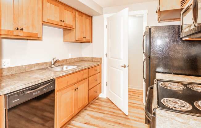 a kitchen with wooden cabinets and black appliances and a door to the refrigerator