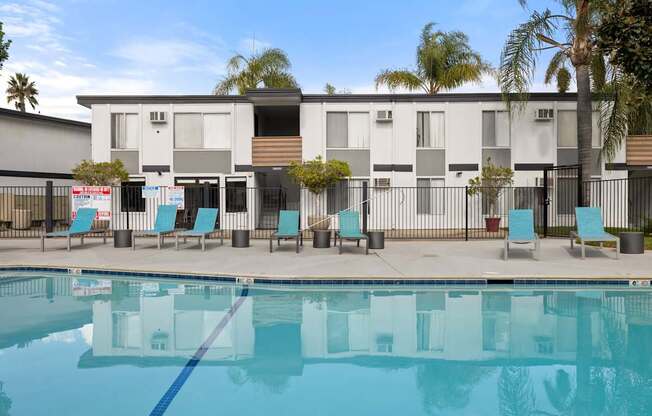 A swimming pool in front of a building with a fence and chairs around it.