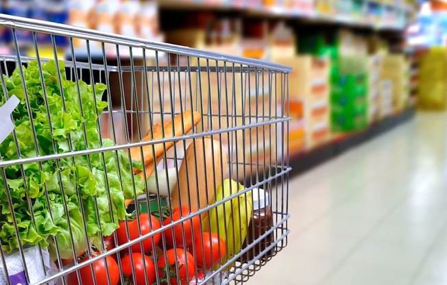 A shopping cart filled with vegetables in a grocery store.