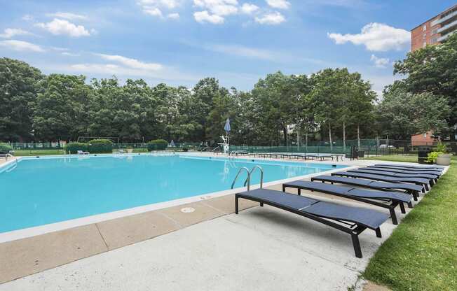 A swimming pool with sun loungers and trees in the background.
