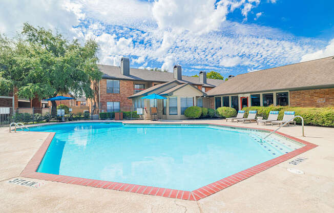 A large swimming pool in front of a house with a red brick exterior.
