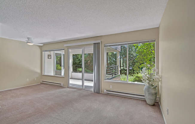 A bright living room here at Watercrest with soft carpet, large windows, and a sliding glass door leading to a private balcony, allowing abundant natural light and creating a peaceful, open atmosphere.