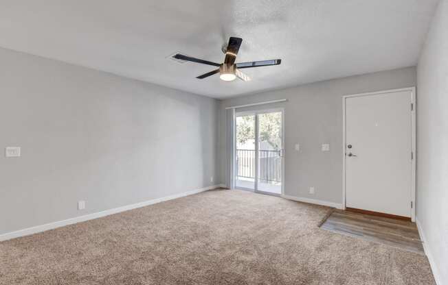 an empty living room with a ceiling fan and a door to a balcony