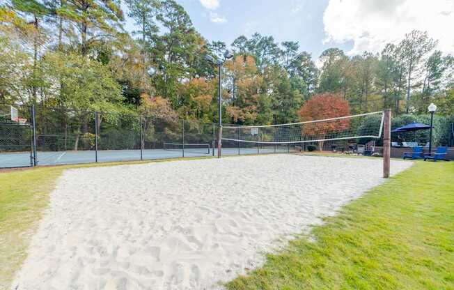 A sandy volleyball court surrounded by a fence and trees.