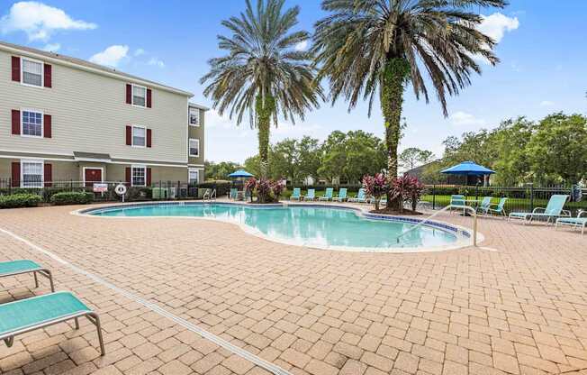 A pool surrounded by a brick patio and palm trees.