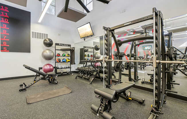 A gym with a weight bench, weights and a wall clock.
