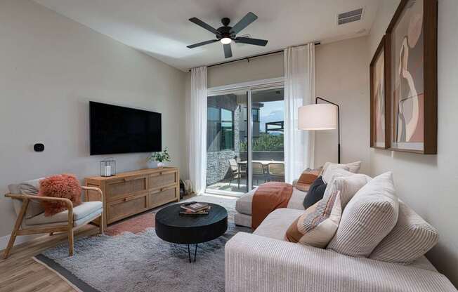 A living room with a white couch, a wooden chair, a black coffee table, and a flat-screen TV mounted on the wall.