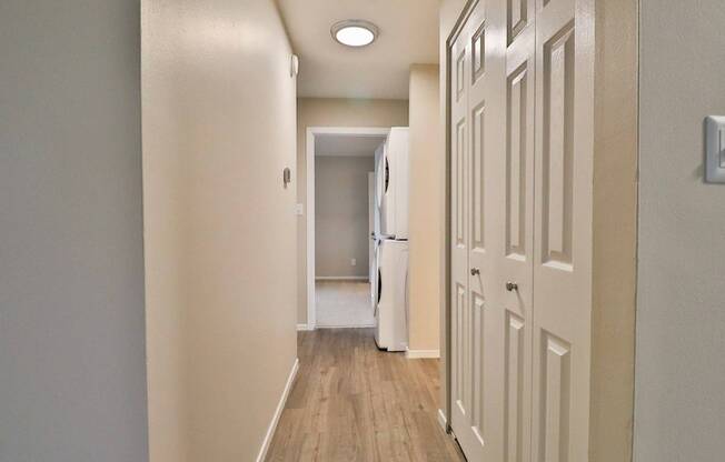 A hallway with a white door on the right and a white fridge in the middle.