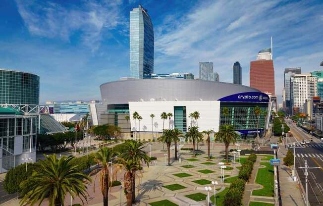 A modern building with a glass facade is surrounded by palm trees and other greenery.
