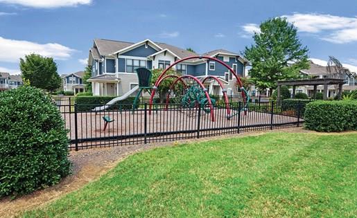 fenced play area with playground equipment next to lawn and apartment buildings