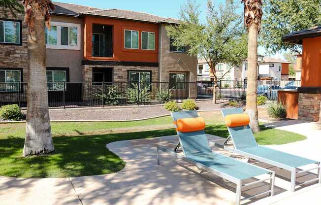 Two lounge chairs sit on a patio in front of a house.