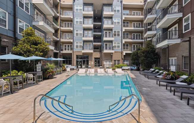 an outdoor swimming pool with lounge chairs and umbrellas in front of an apartment building