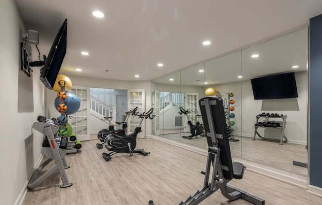 A well-equipped home gym with various exercise machines and a flat-screen TV mounted on the wall.