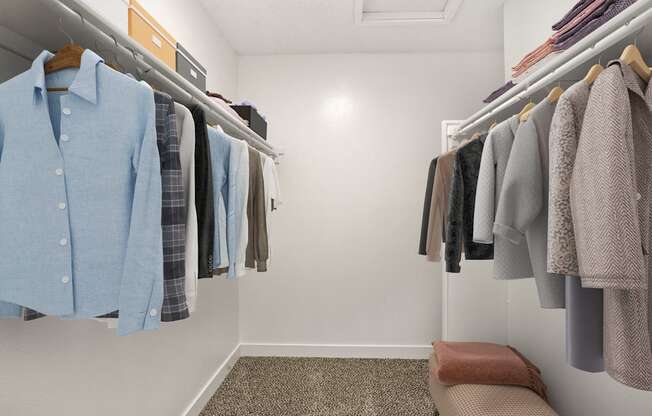 A white closet with clothes hanging on shelves and a bench at the end.
