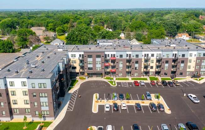an aerial view of a large apartment complex with a parking lot and trees in the background