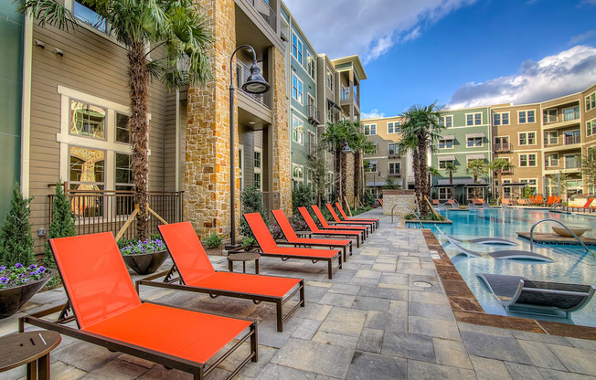 an outdoor swimming pool with chaise lounge chairs and palm trees in front of an apartment building