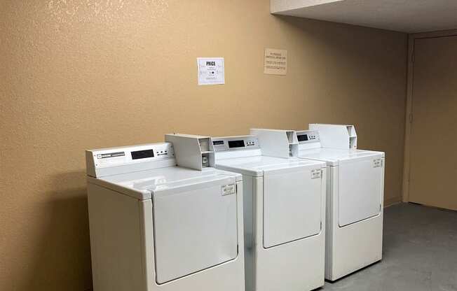 Three washing machines are lined up in a laundry room.