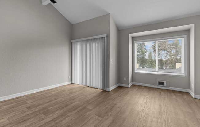 an empty living room with a large window and wood flooring