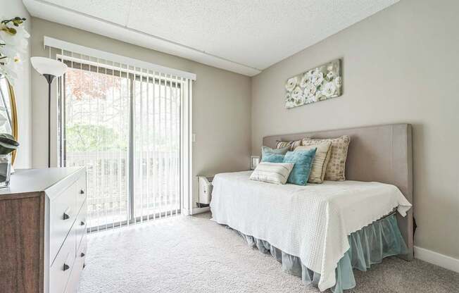 A bedroom with a bed, dresser, and window with blinds.