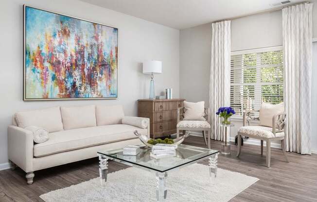 A living room with a white couch, a glass coffee table, and a colorful painting on the wall.