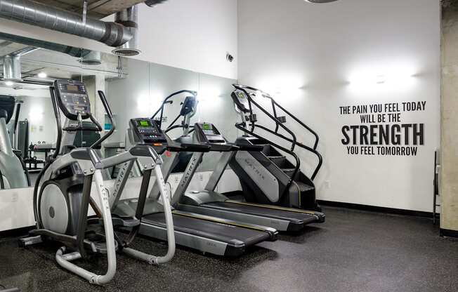 a row of treadmills in a gym with a wall quote from the gym