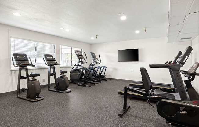 A gym with a row of exercise bikes and a television mounted on the wall.