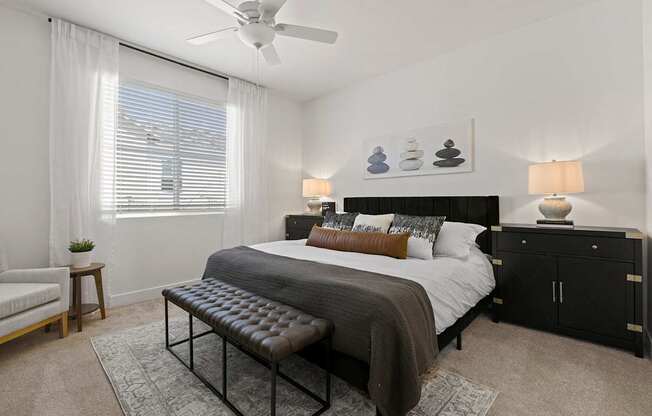 A bedroom with a large bed, a bench, and a ceiling fan.