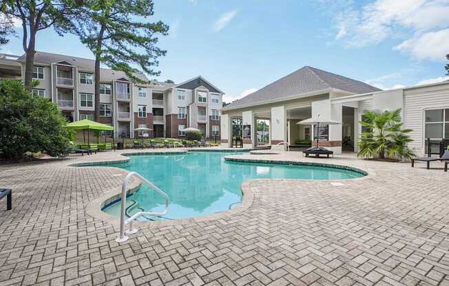 A swimming pool surrounded by a brick patio and apartment buildings at The Falls Apartments in Raleigh NC