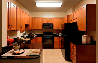 Warm & Inviting Kitchen With Wooden Cabinetry, Black Appliances, & Granite Countertops