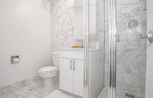 A bathroom with white cabinet and toilet and marble walls