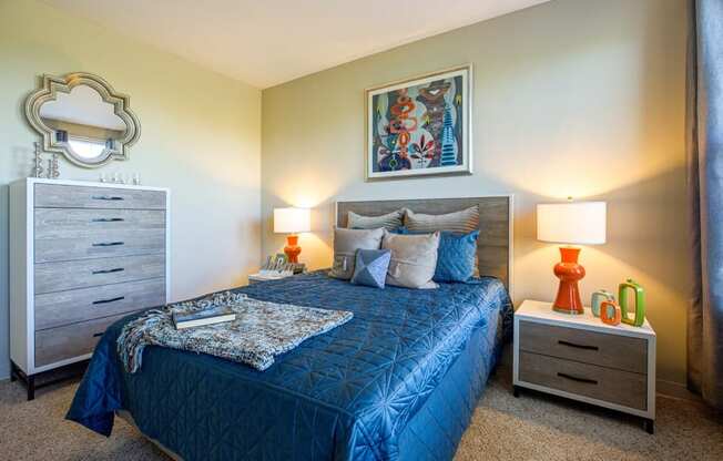 A bedroom with a blue bedspread and a painting on the wall.