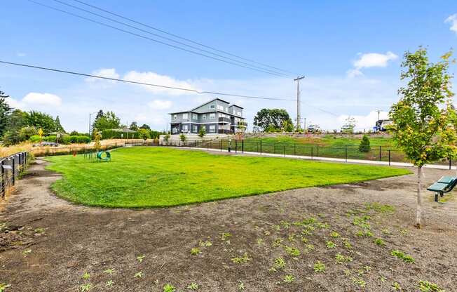 A large grassy field with a fence and a house in the background.