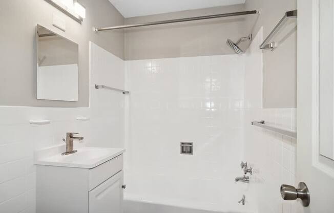 A white bathroom with a sink, mirror, and shower.