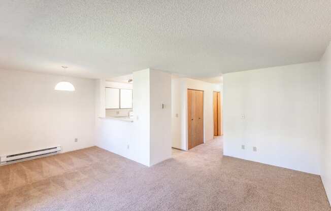 an empty living room with a kitchen in the background