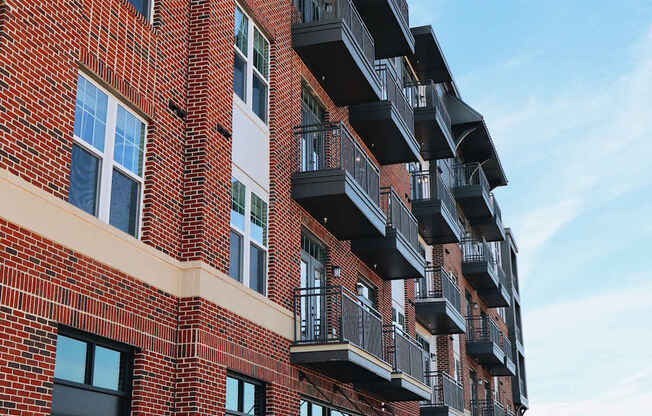 A red brick building with balconies and a black gate in front.