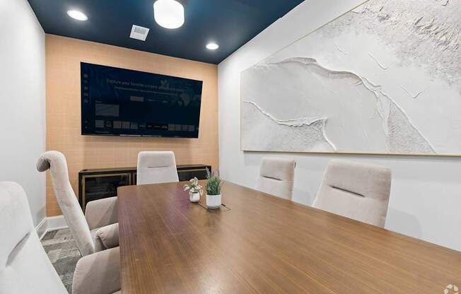 A conference room with a wooden table, chairs, and a large screen on the wall.