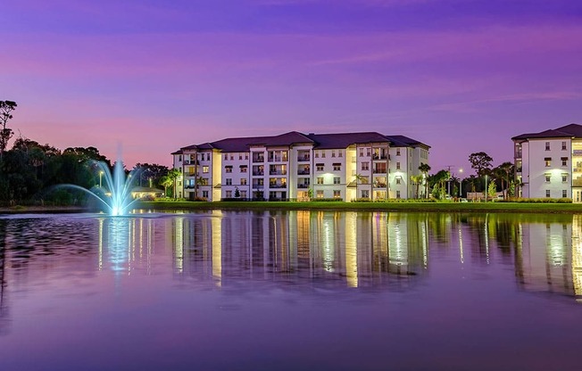 a fountain in a lake with an apartment building at dusk