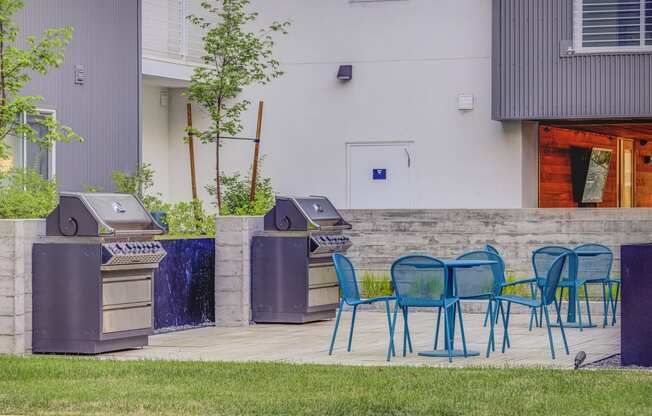 two bbq grills and blue chairs on a patio in front of a building