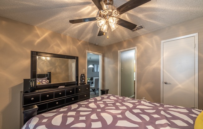 A bedroom with a bed, dresser, mirror, and ceiling fan.