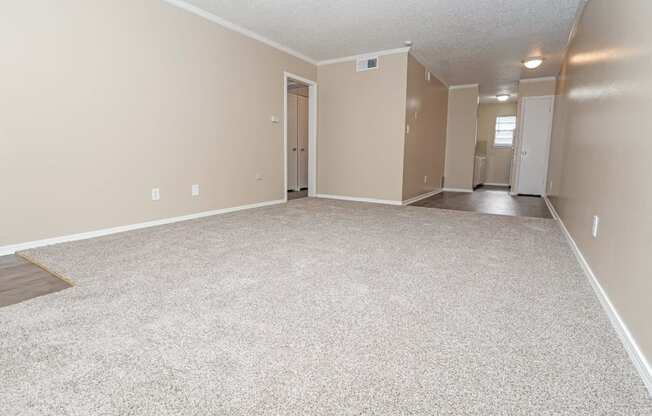 A spacious carpeted living room that leads to the kitchen  at The Creole Apartments in Shreveport, LA