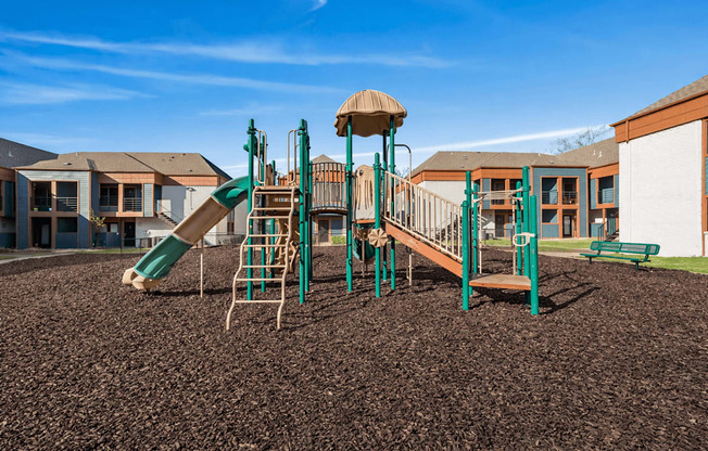 A playground with a green slide and a brown sandbox.